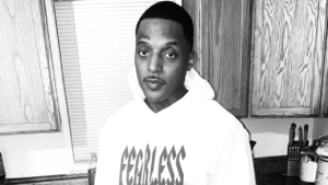 B&W photo of Chicago rapper FBG Cash looking at camera wearing white hoodie with 'FEARLESS' in gothic red lettering across chest